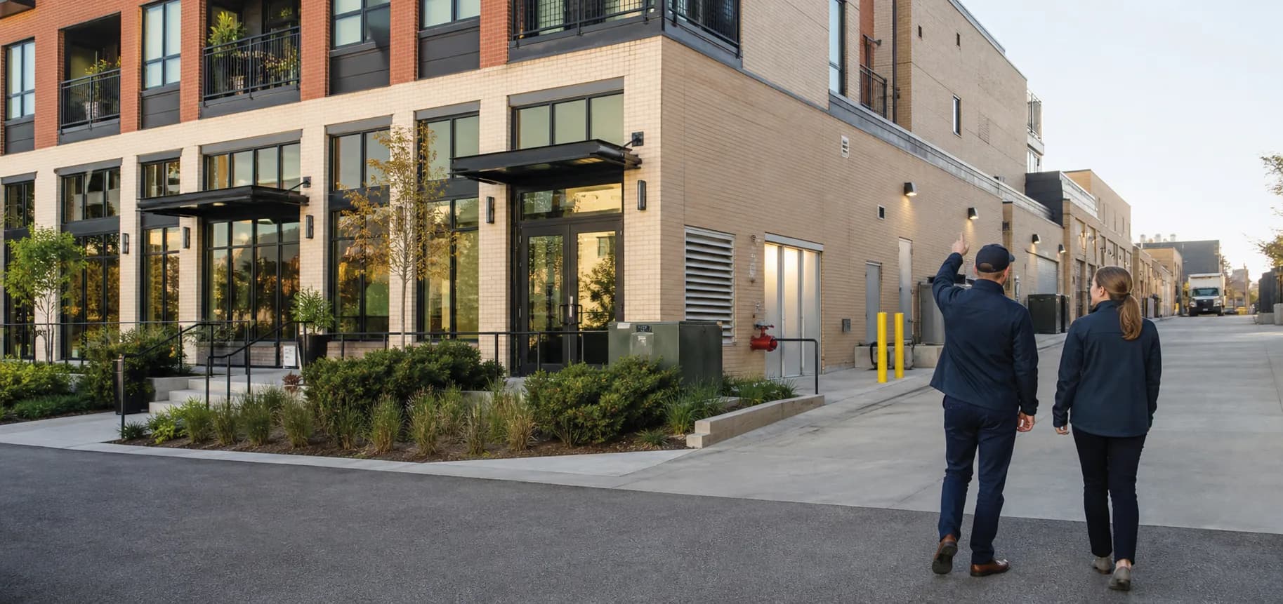 Property manager and building engineer walking the service side of a mixed-use commercial property while reviewing its exterior systems