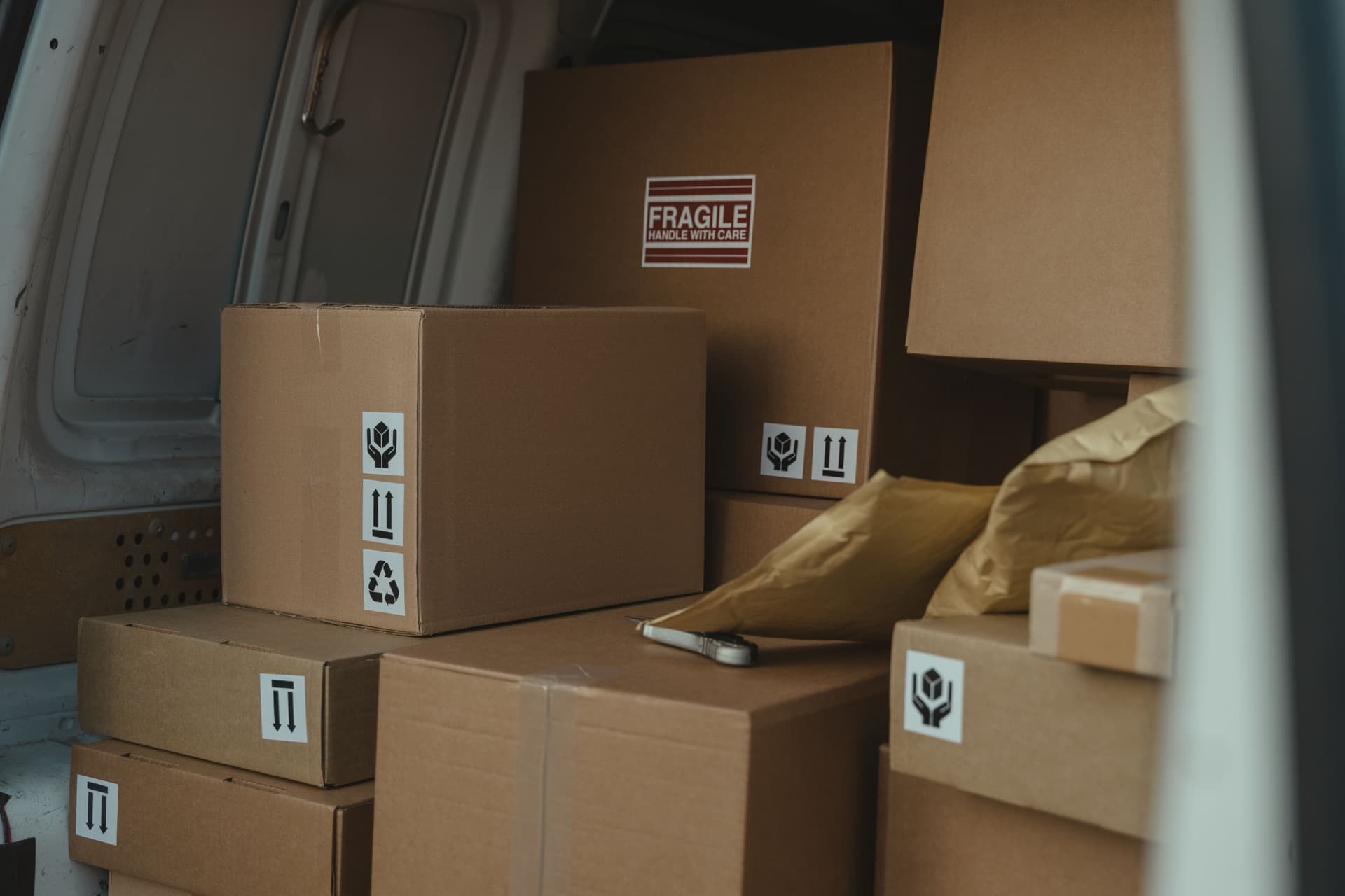Interior of a white cargo delivery van packed with stacked cardboard boxes and padded mailers ready for parcel routes