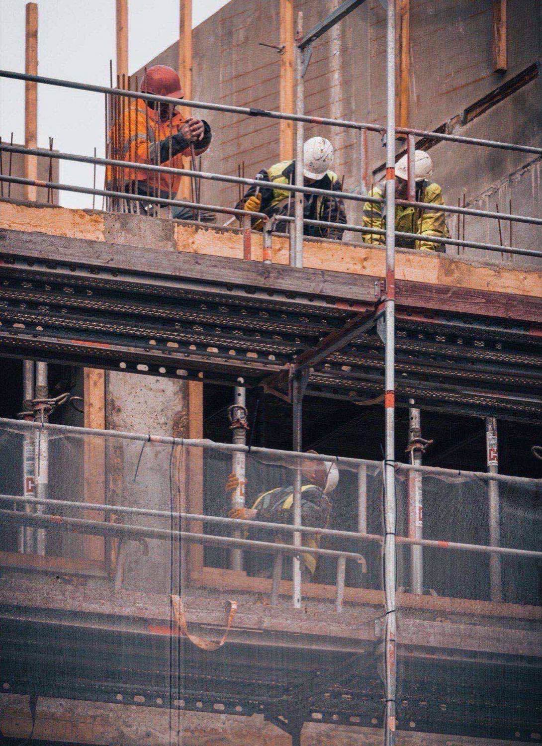 Construction workers in hard hats and safety vests on multi-level steel scaffolding at a building framing site