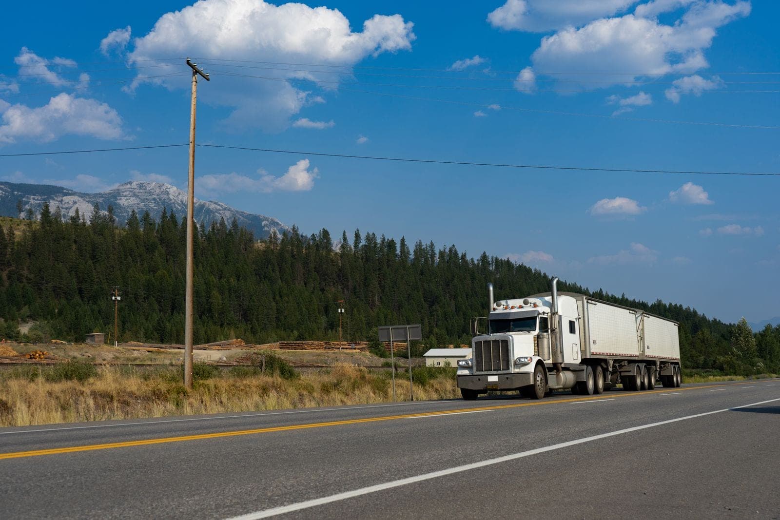 White commercial semi-truck hauling a bulk trailer along a mountain highway, a long-haul over-the-road trucking operation