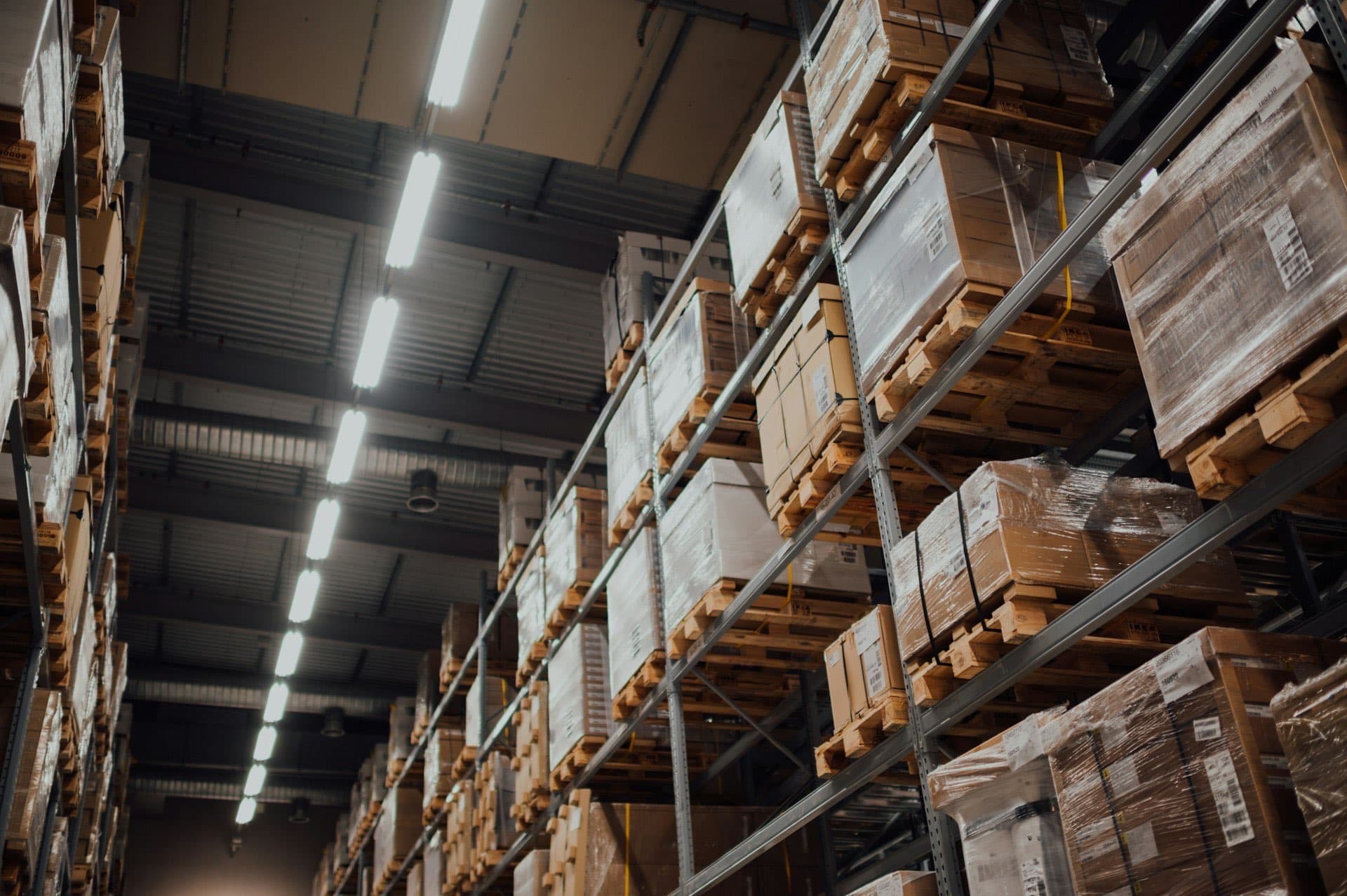 High-bay wholesale warehouse with metal racking stacked with palletized cardboard cartons under industrial ceiling lights